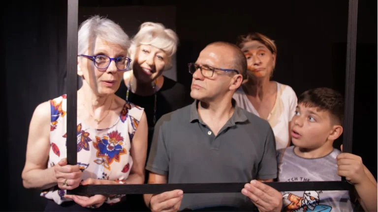 Cinque persone di diverse età guardano attraverso una grande cornice nera con espressioni curiose e teatrali.