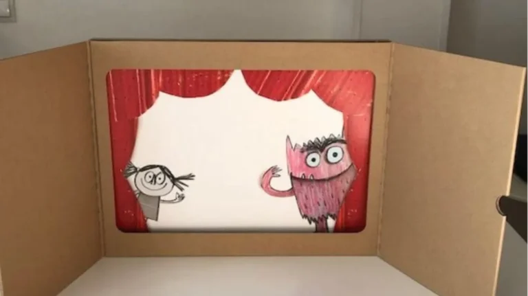 Teatrino di cartone fai da te per bambini con tende rosse e due personaggi disegnati: una bambina e un mostro rosa.